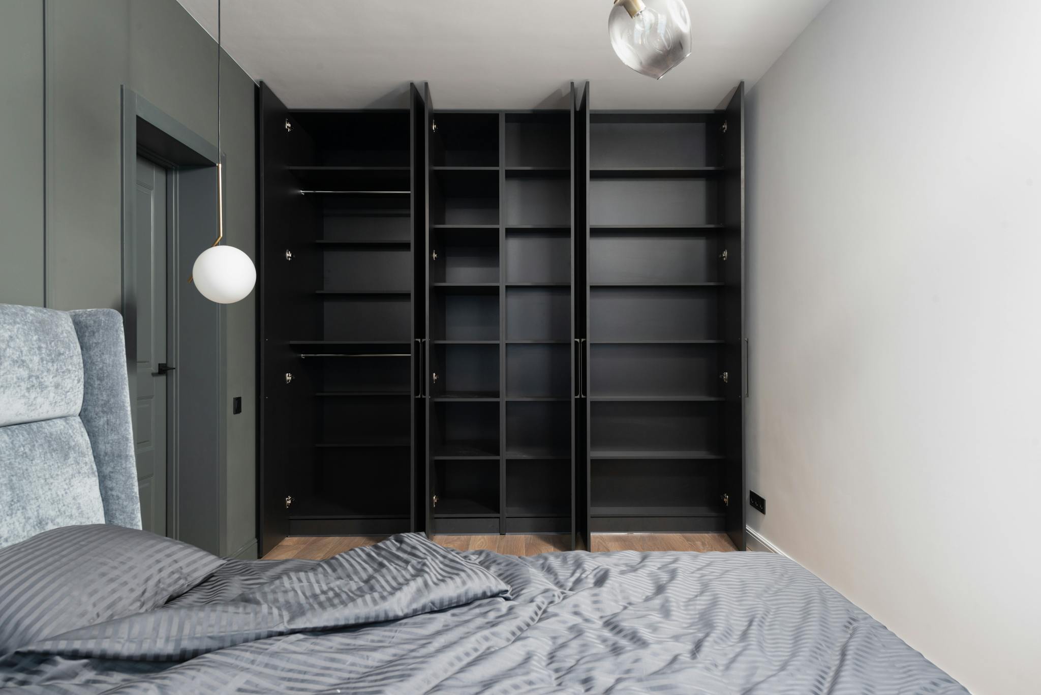 Contemporary bedroom interior with open black wardrobes and minimalist design elements.